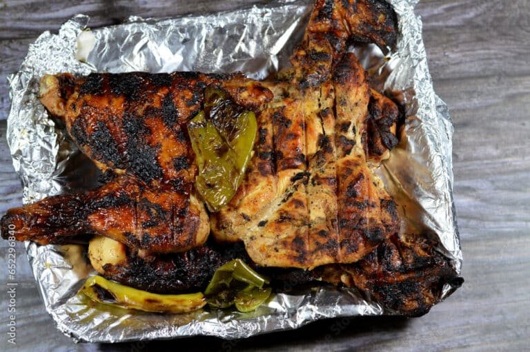 Chicken grilled and roasted on a charcoal grill, served on a disposable plate with grilled green peppers and bell peppers, chicken meat grill, Mesahab cooked on charcoal, isolated on wooden background